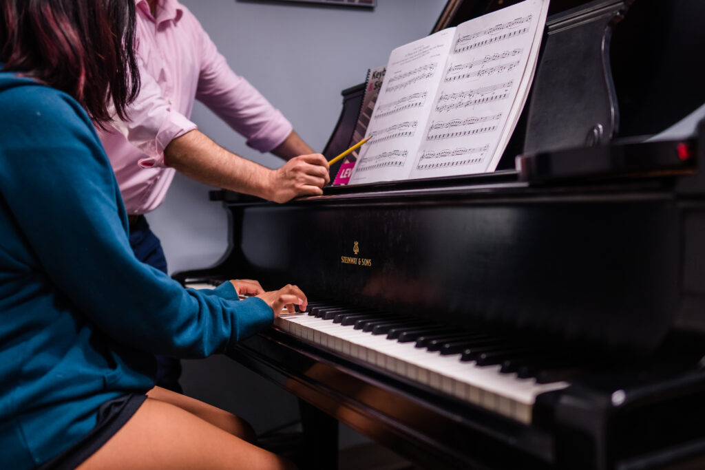 Instructor pointing toward sheet music while student plays piano