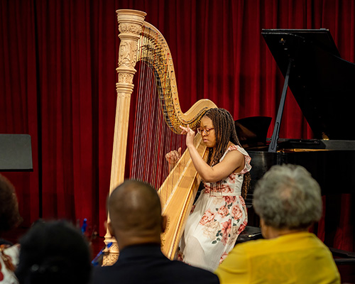 Student playing a harp in a recital.