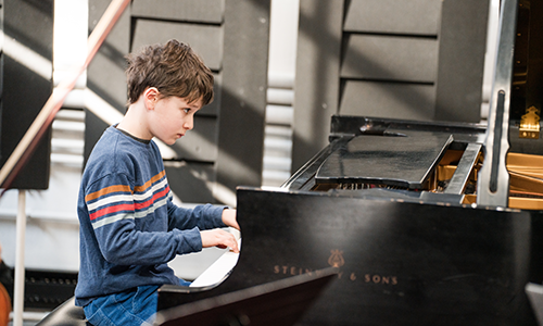 Young male Suzuki piano student sitting at a grand piano.