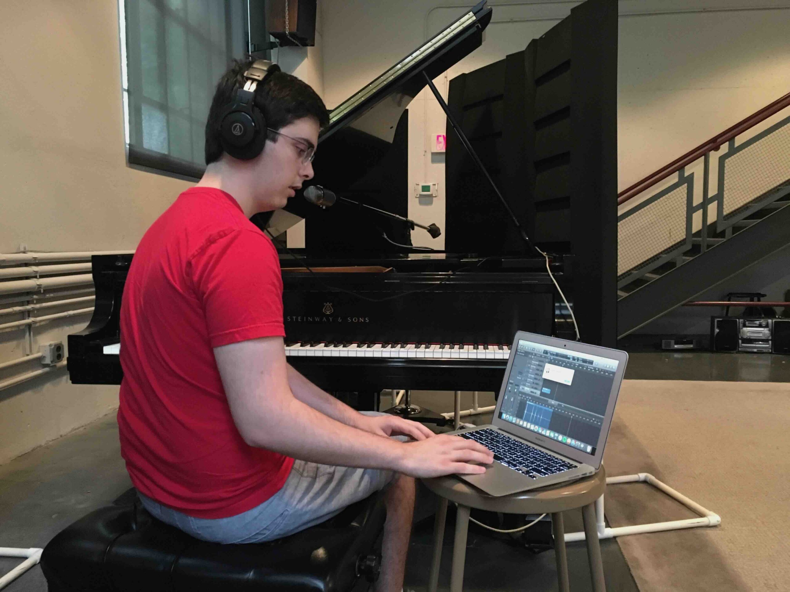 A student working on a music production project while sitting at a piano.