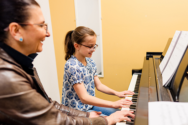 Female piano instructor smiling while teaching a student at the piano.