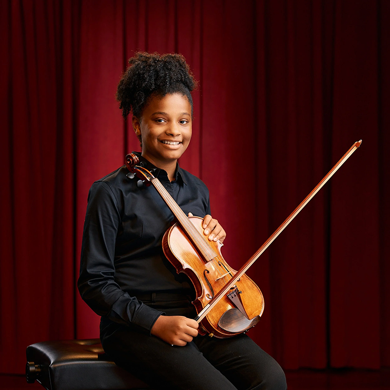 Photo of Aidyn Ellis-Otova seated holding a violin.