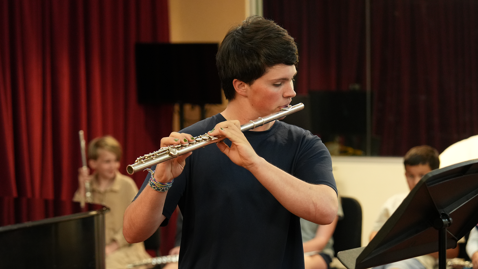 A male teen student playing the flute with students in the background.